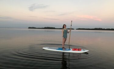 A woman on a paddle board holding a paddle at dusk